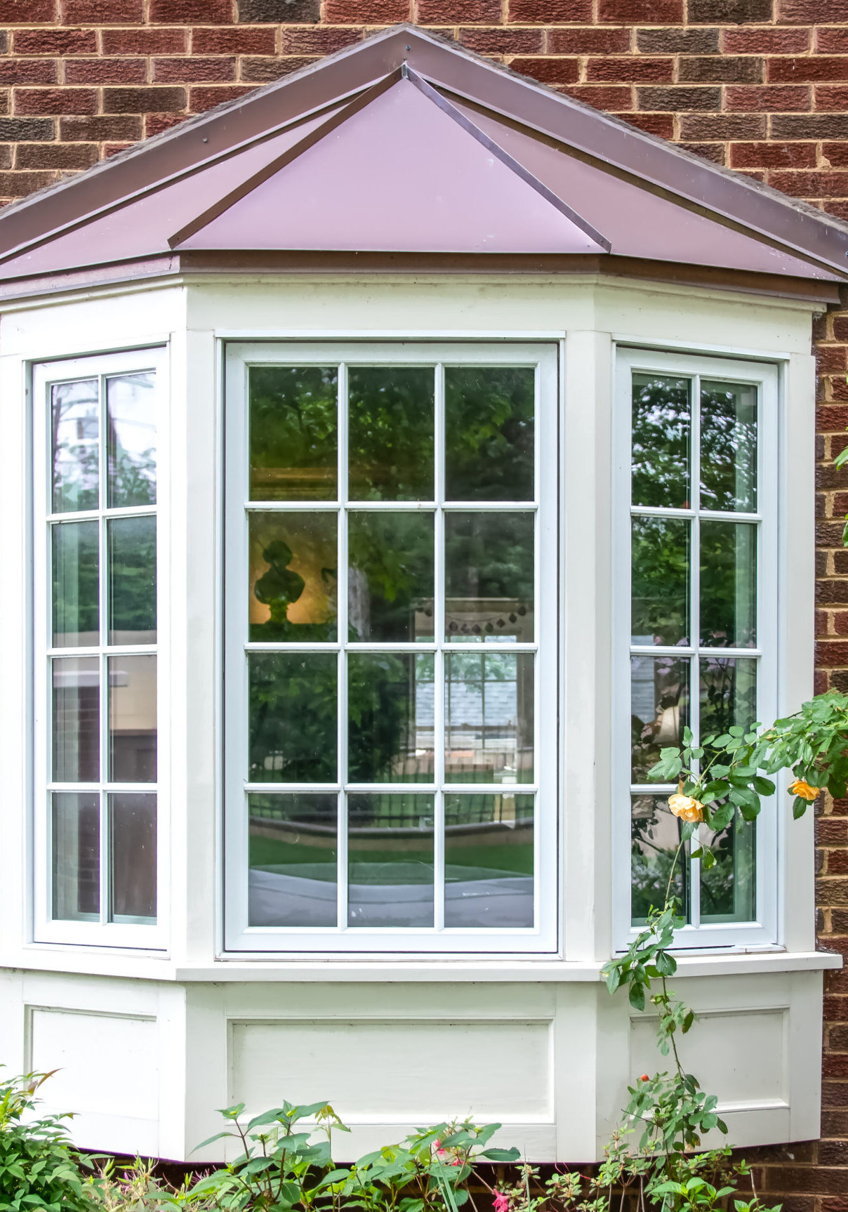 Bay window with copper roof on traditional brick home with flowe Bay window with copper roof on traditional brick home with flowers below and yellow roses extending out onto the window in springtime